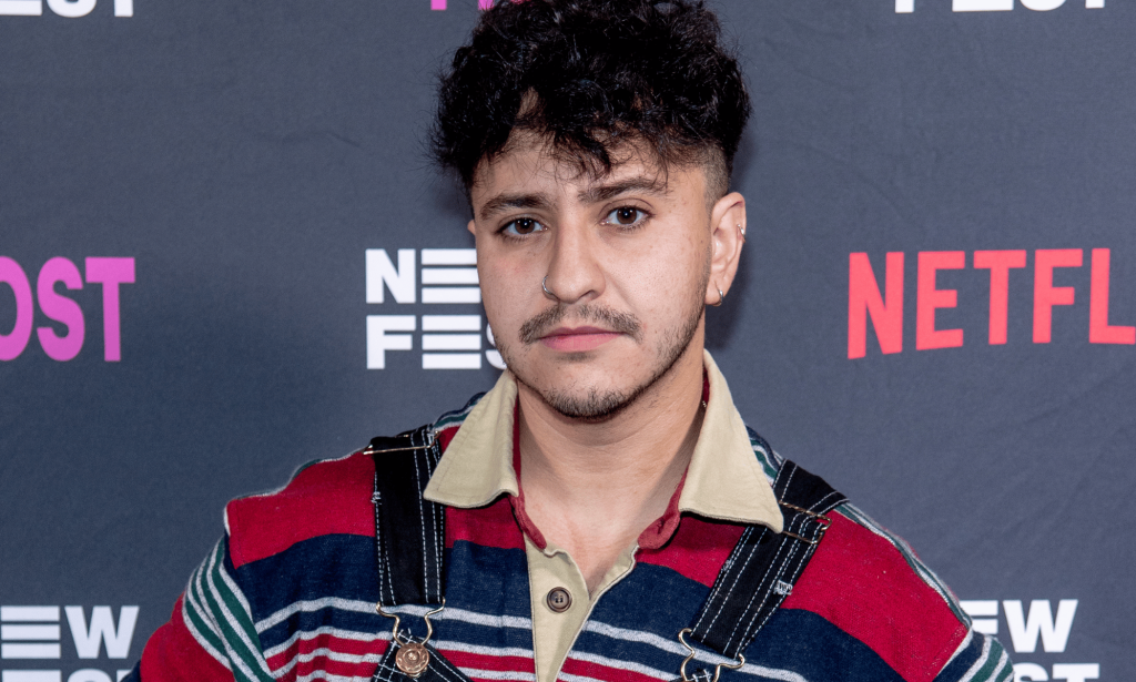 Zach Barack wears a striped shirt as he stands in front of a background with the Netflix logo on it