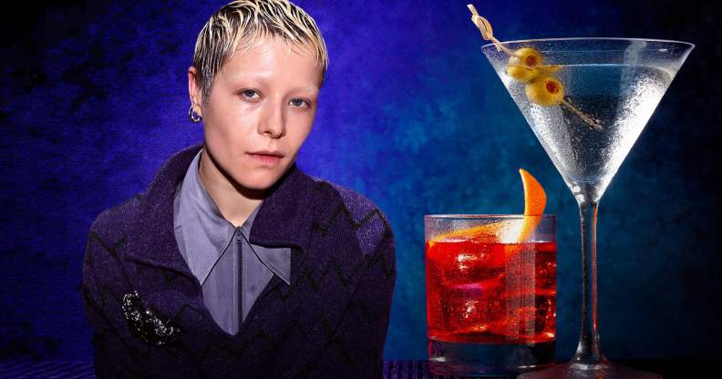 A photo of actor Emma D'Arcy sitting next to two drinks that are placed on a table