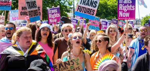 A large group of people holding pro-trans signs march through London during a Trans+ Pride march