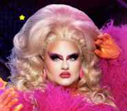 A promotional photo of Victoria Scone in full pink drag outfit with spotlight graphics shining in the background