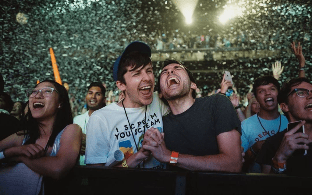 God of War: Ragnarok developers Sam Handrick and Jake Snipes celebrating in a live performance venue, surrounded by confetti amid a cheering a crowd.