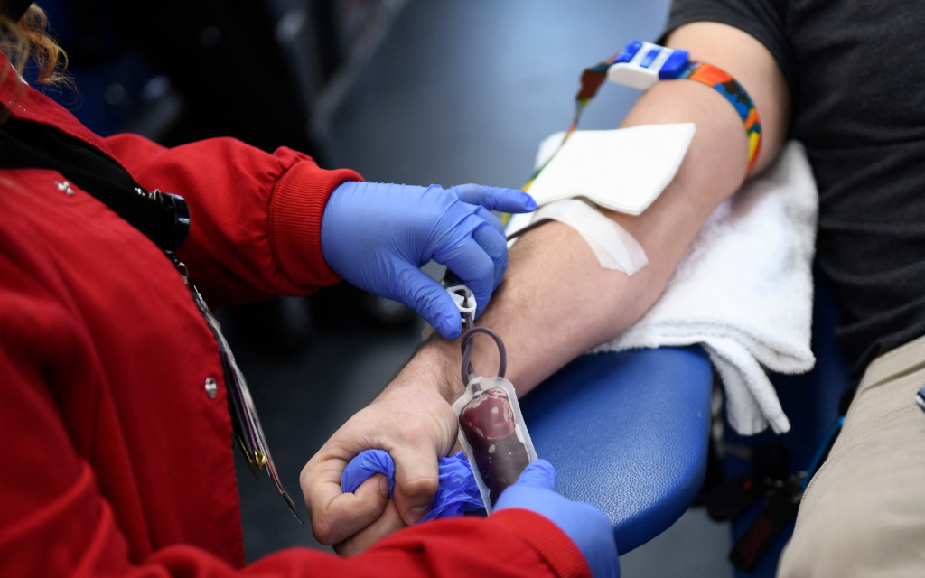 A picture of an individual's arm as they are donating blood, with a professional in blue latex gloves presiding over the operation.