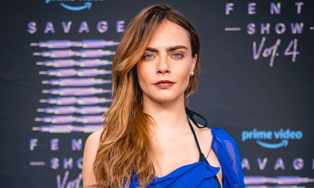 Cara Delevingne in a blue top, centre of the camera looking forward.