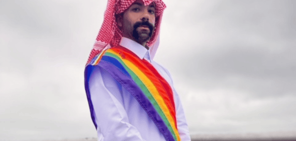 Dr Nas Mohamed wears Qatari attire with a sash in the colours of the LGBTQ+ Pride flag