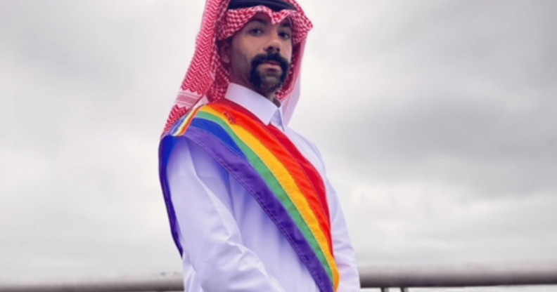 Dr Nas Mohamed wears Qatari attire with a sash in the colours of the LGBTQ+ Pride flag