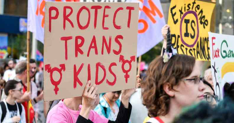 A photo shows a group of trans activists protesting, one sign being held says "Protect Trans Kids".