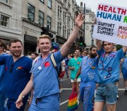 A group of NHS England doctors march during a Pride parade. One is wearing a sign that reads: "HEALTH IS A HUMAN RIGHT. Support Migrants, Support Trans PPL, Support PrEP"