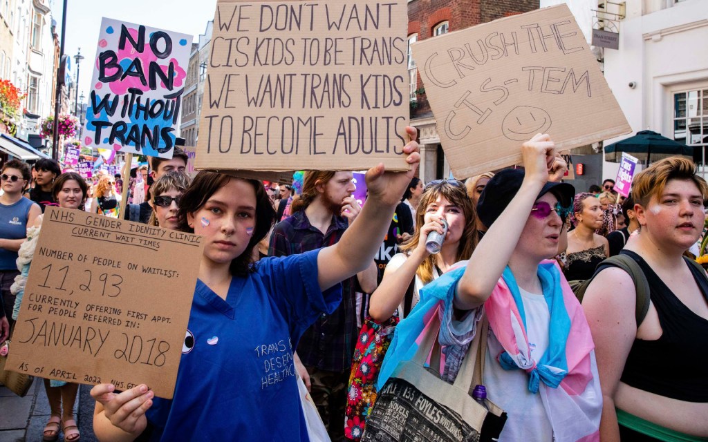An individual wearing NHS England clothes waves signs detailing the amount of people on the GIC waitlist as of April 2022. 