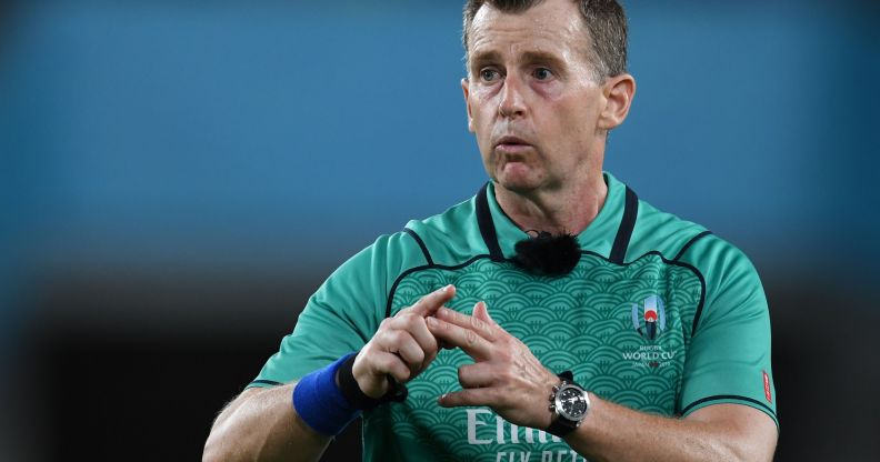Nigel Owens makes a gesture while refereeing a rugby match in a green shirt.