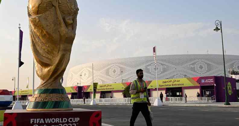 A stadium worker walks past a large statue of the World Cup in Qatar