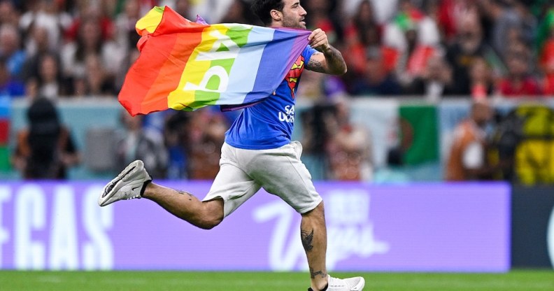 The Qatar World Cup pitch invader runs across the pitch, holding a Pride flag like a cape