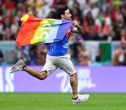 The Qatar World Cup pitch invader runs across the pitch, holding a Pride flag like a cape