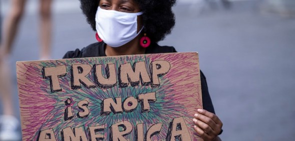 A protester wearing a face mask holds a homemade sign that says, "Trump is Not America"