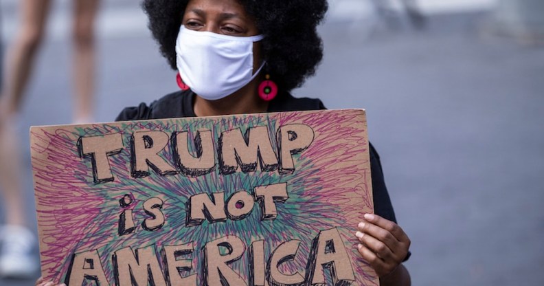 A protester wearing a face mask holds a homemade sign that says, "Trump is Not America"