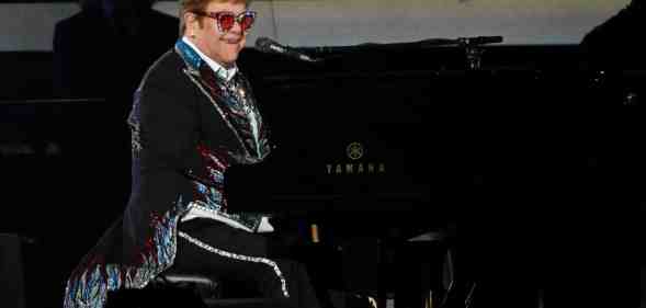 Elton John sitting at a piano in a sparkly blazer
