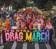 A photo of pro-drag march with people at the front of the crowd holding a banner with the slogan "It's still just a drag march, you may applaud".