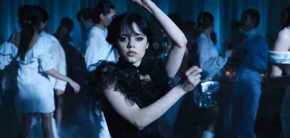 A still from Netflix's Wednesday series showing actor Jenna Ortega as Wednesday Addams dressed in a black dress and holding a dance pose