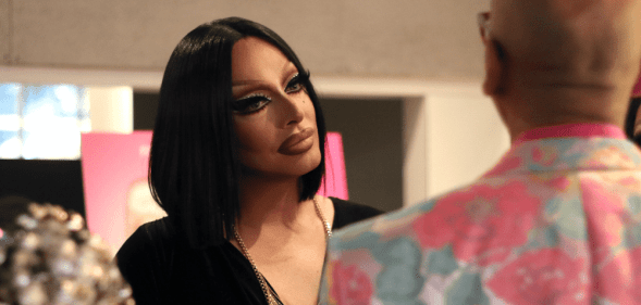 A screenshot of Drag Queen's Raven wearing a black dress talking to RuPaul who is standing with his back to the camera wearing a floral patterned suit jacket