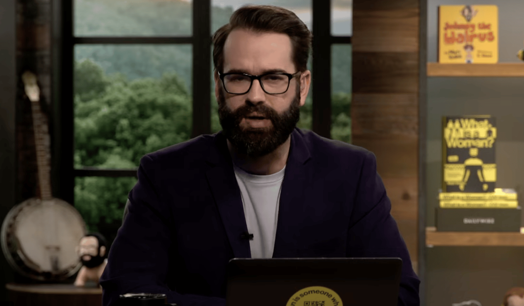 A screenshot of right-wing columnist and blogger Matt Walsh wearing glasses, black suit jacket over a white T-shirt talking on his YouTube show