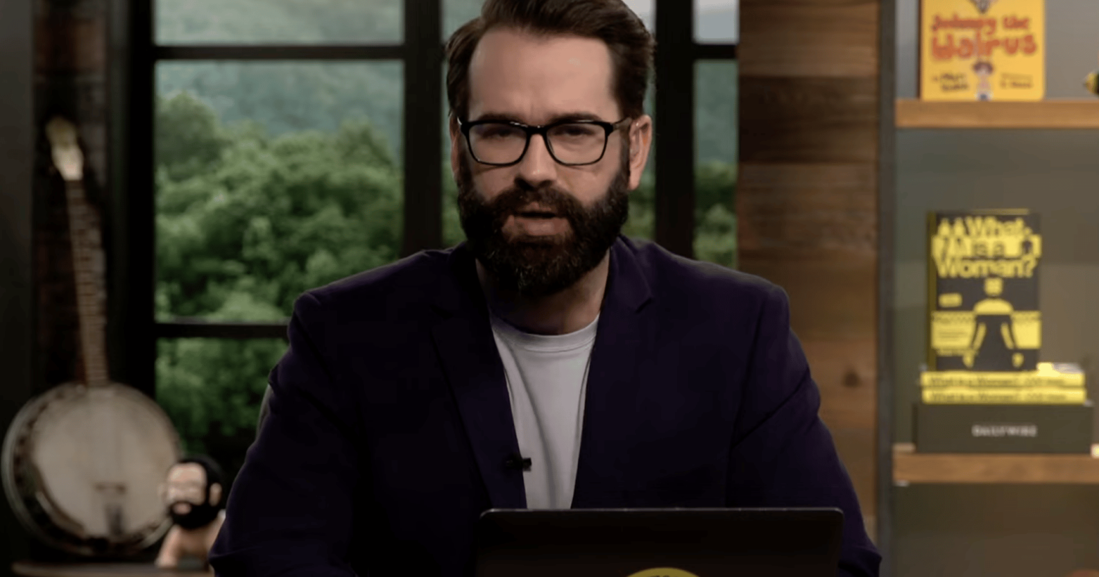 A screenshot of right-wing columnist and blogger Matt Walsh wearing glasses, black suit jacket over a white T-shirt talking on his YouTube show