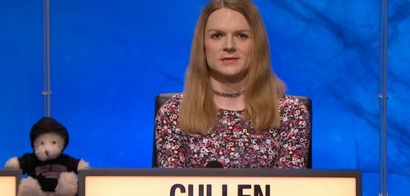 Emily Cullen appears on university challenge against a blue background, next to the team's teddy bear mascot