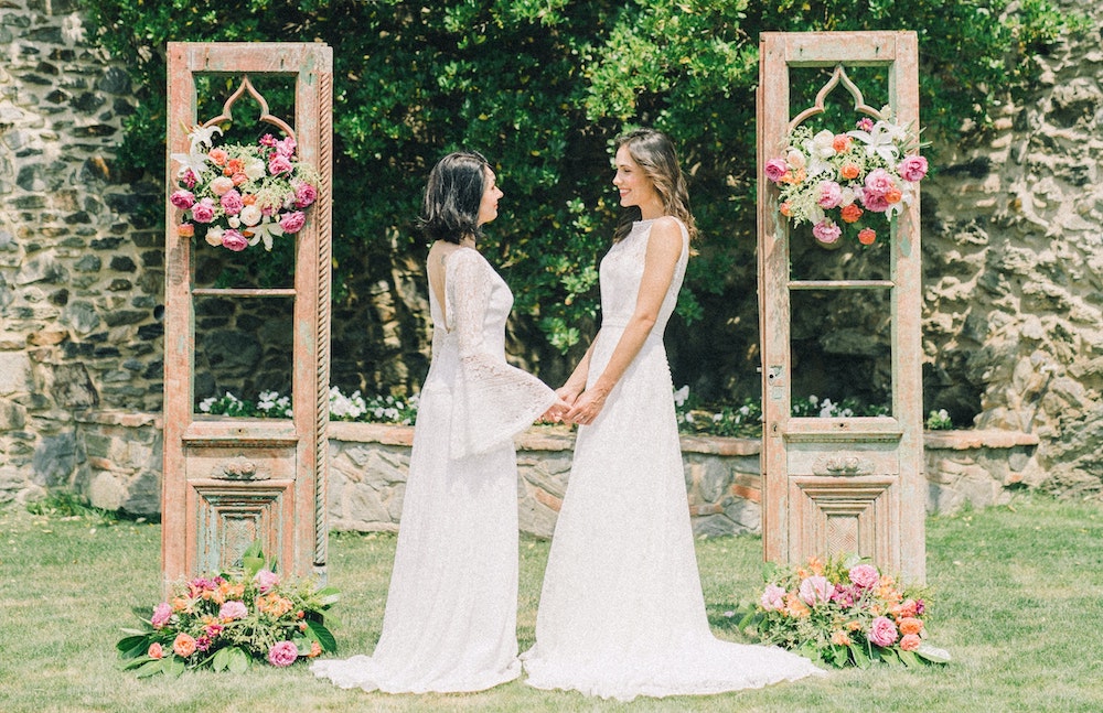 A same-sex couple gets married outside in white dresses