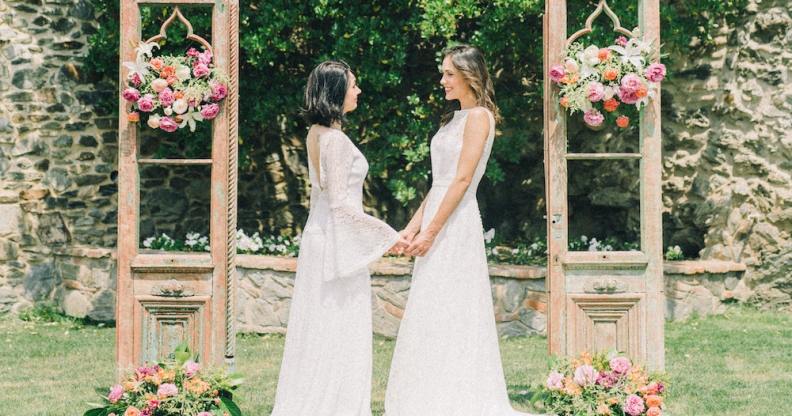 A same-sex couple gets married outside in white dresses