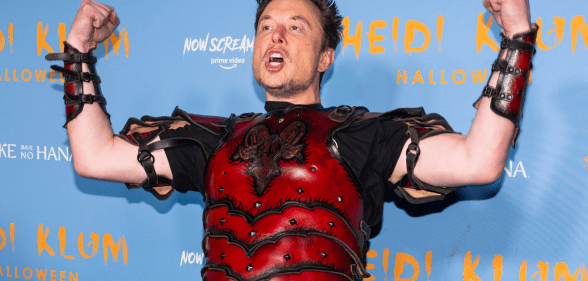 Elon Musk flexes while wearing a set of read armour during a Haloween christmas party.