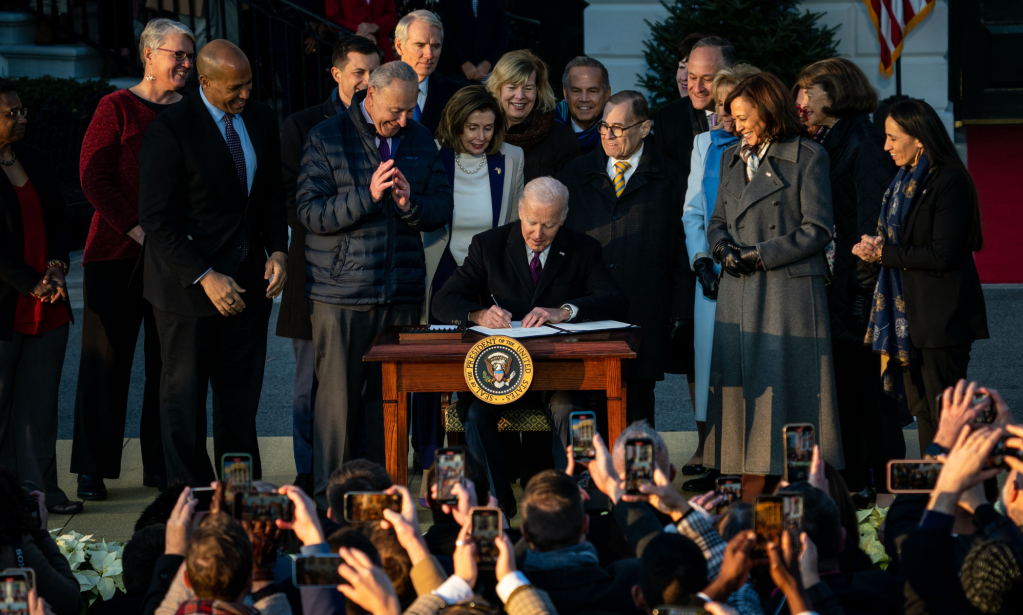 Joe Biden, surrounded by politicians and activists, puts pen to paper on a White House table to sign the Respect for Marriage Act.