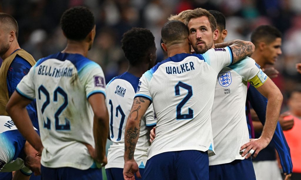 Harry Kane is embraced by a football player while surrounded by players still weirdin their white England kits.