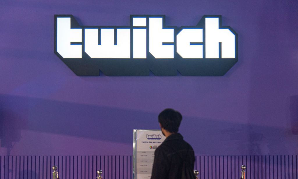 An individual stares at a plaque below a giant Twitch logo offset on a massive purple wall.