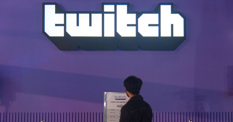 An individual stares at a plaque below a giant Twitch logo offset on a massive purple wall.