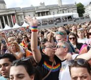 A crowded group sees two people kiss each other while raising their hands during the Pride in London parade