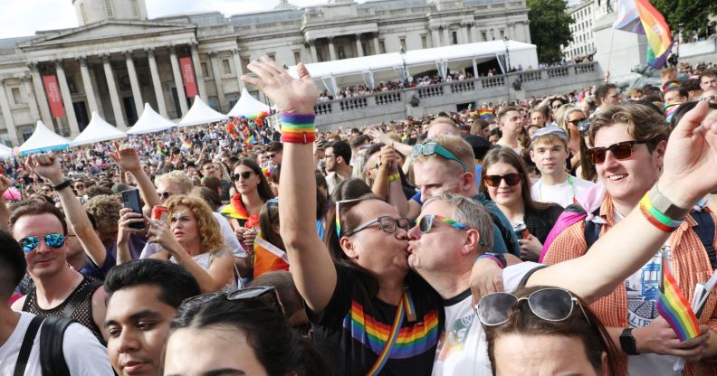 A crowded group sees two people kiss each other while raising their hands during the Pride in London parade