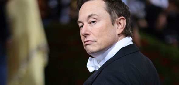 Elon Musk turns his head, eyebrow raised, giving a stern look to the camera.