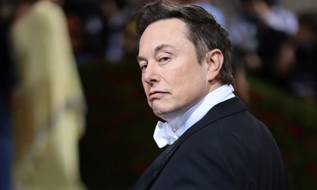 Elon Musk turns his head, eyebrow raised, giving a stern look to the camera.