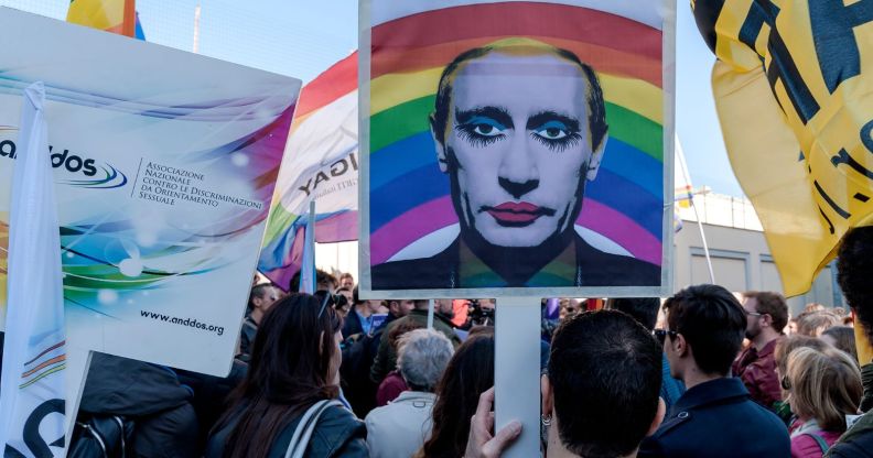 Several protestors march down a street, as a member of the public holds up a picture of Vladimir Putin, edited so that he is wearing makeup.