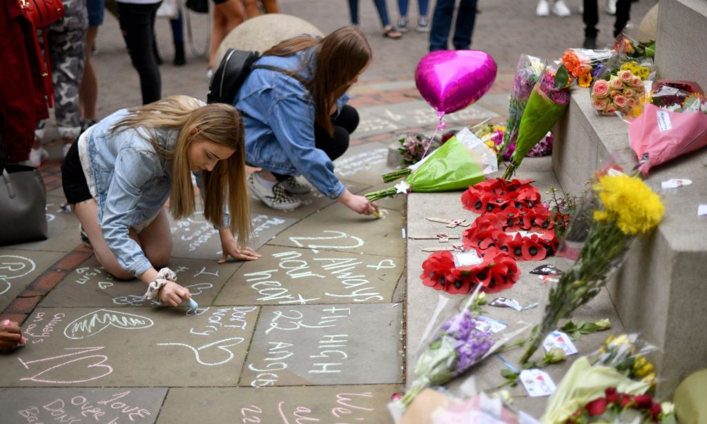 Two people crouched down writing messages of solidarity in chalk surrounded by flowers.