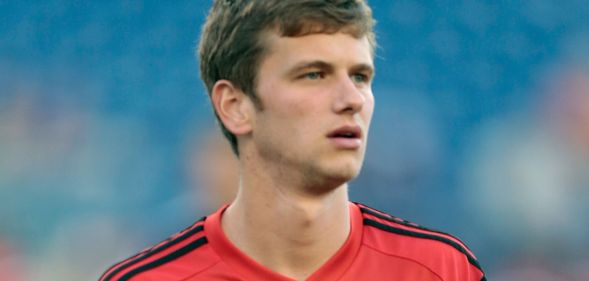 Collin Martin, wearing a red shirt, stands on the pitch of a football stadium.