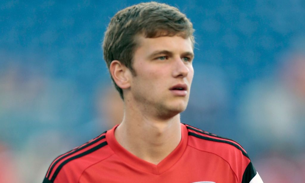 Collin Martin, wearing a red shirt, stands on the pitch of a football stadium.