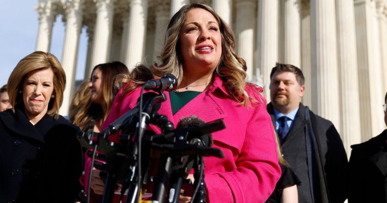 Lorie Smith, in a pink jacket, speaks outside the Supreme Court, with an array of microphones in front of her.