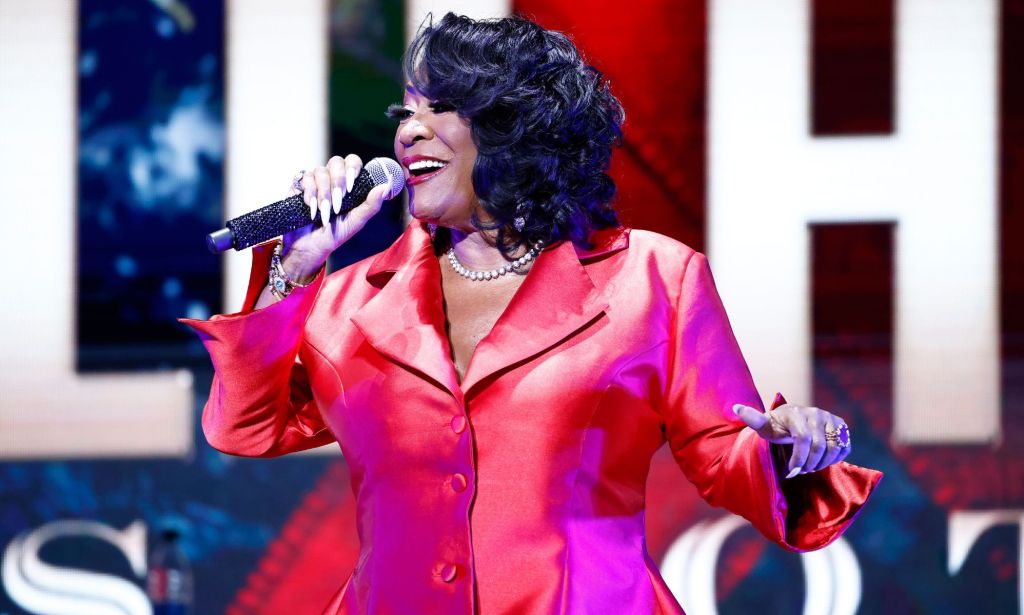 Patti LaBelle sings in a red dress while on stage while a partial graphic for World AIDS Day comes into view behind her.