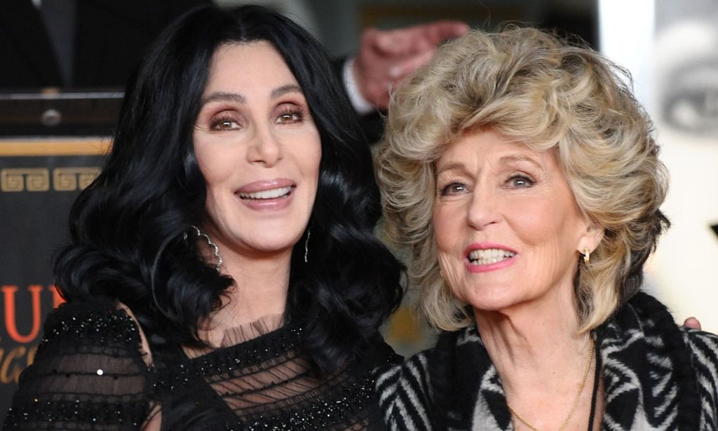 Cher, wearing a black dress, holds her mother, who is wearing a grey striped suit.