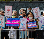 Members of a pro-LGBTQ+ protest wave trans-positive signs, as well as the pink, blue, and white trans flag.
