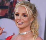 Britney spears, smiling and wearing a red dress, waves at onlookers as she walks past.