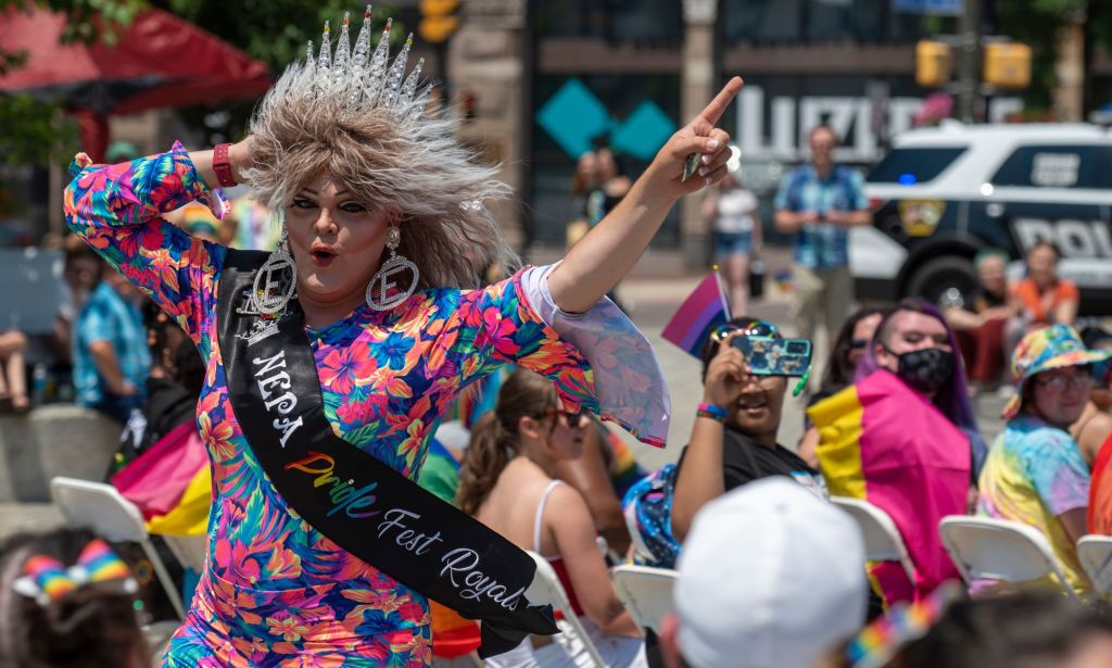 A drag queern points her finger into the air while celebrating at a Pride event.