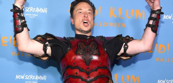 Elon Musk, wearing a red suit of armour, raises his arms and screams.