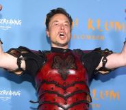 Elon Musk, wearing a red suit of armour, raises his arms and screams.