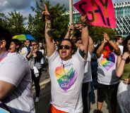 A person in a Pride shirt screams while pointing a finger in the air and holding a sign that reads "gay"