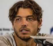 Taylor Fritz, wearing a white tee, speaks during a press conference into a small microphone.